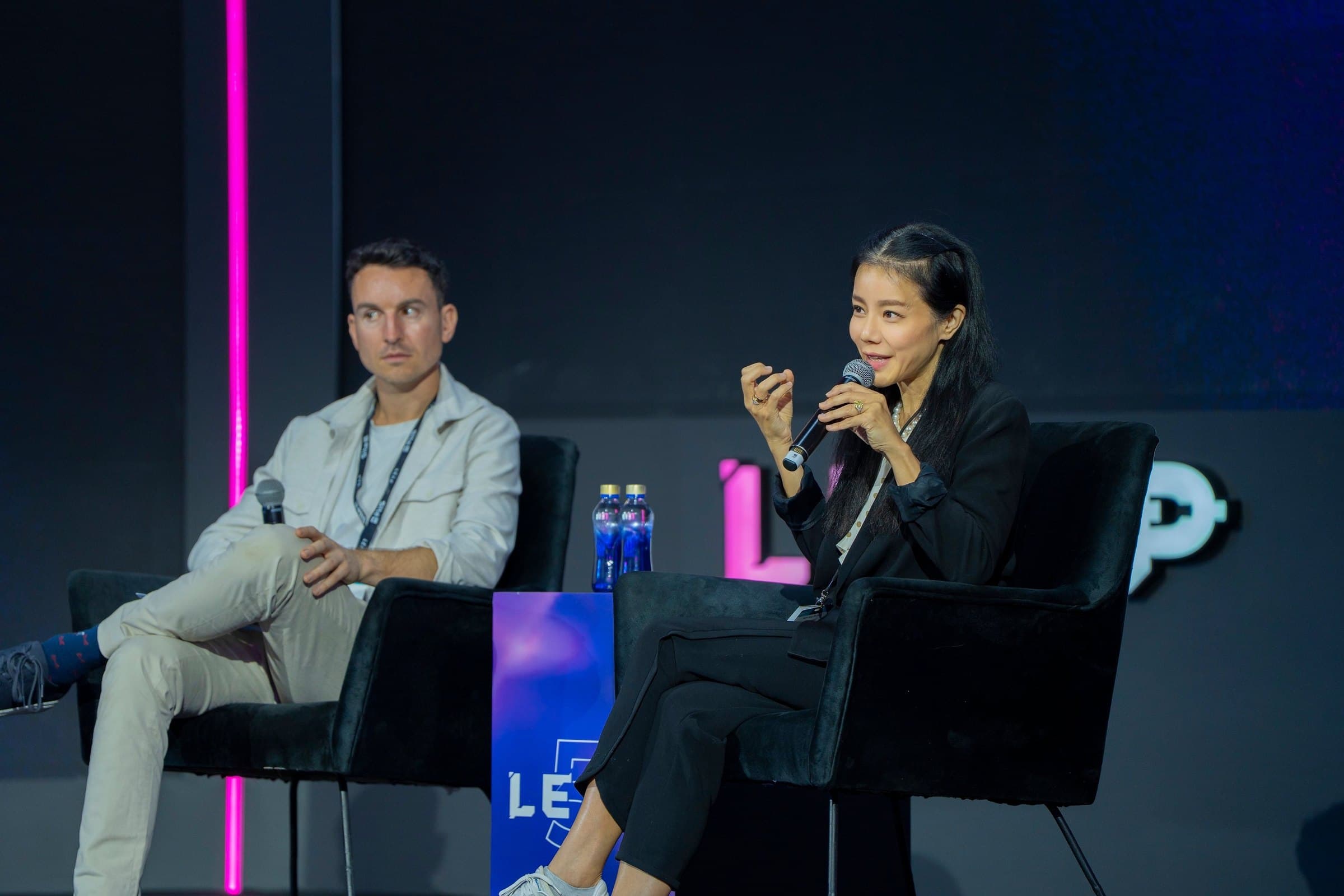 Esther Wong speaking into a microphone on a LEAP panel stage, seated beside a fellow panellist in front of the LEAP logo