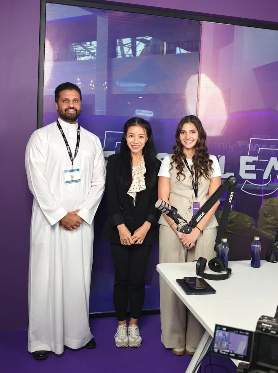 Esther Wong with two members of the LEAP podcast team, standing beside a studio microphone in front of the LEAP backdrop